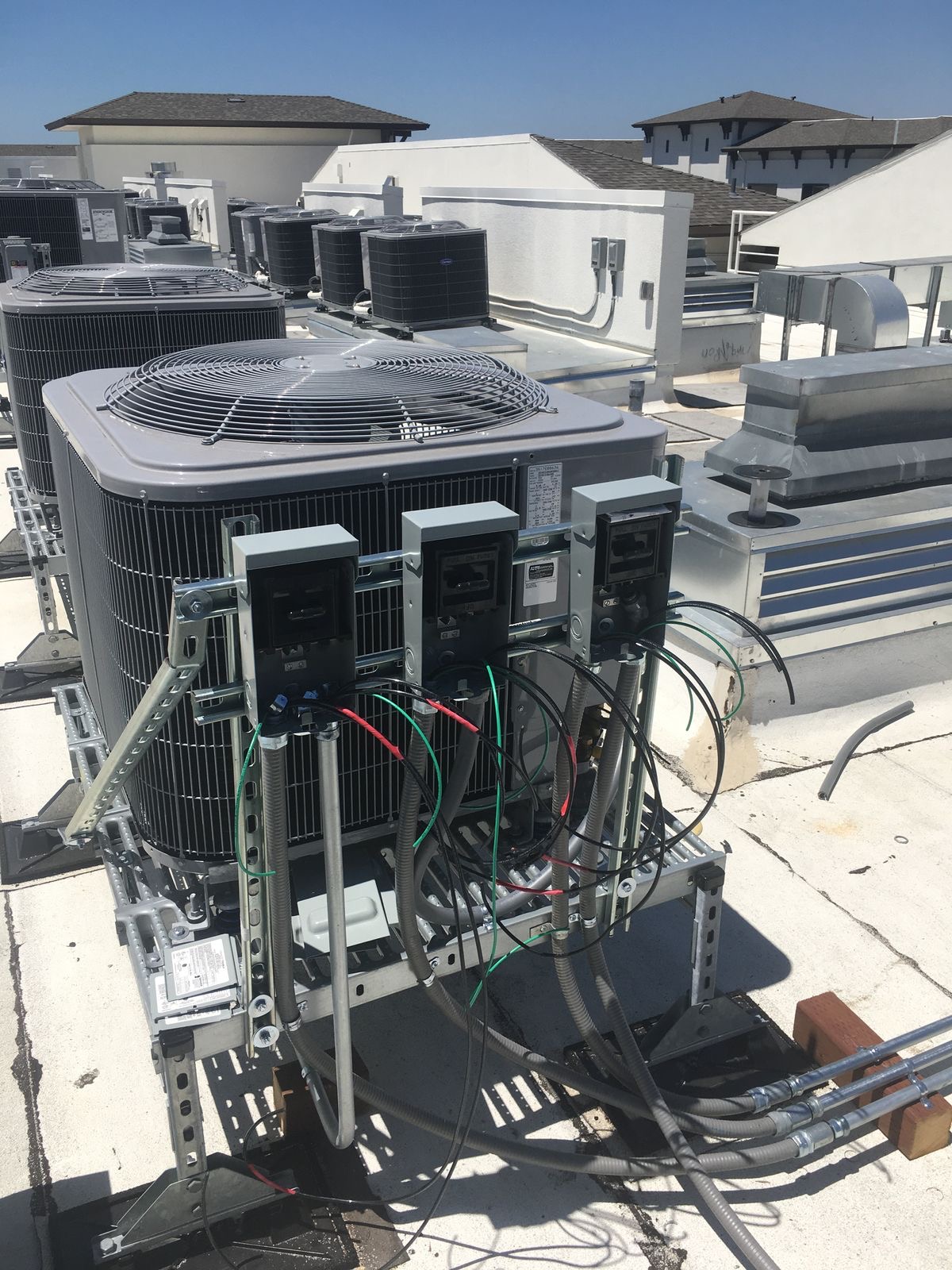 Rooftop bank of air-conditioning condensers wired to new electrical isolators and conduit.